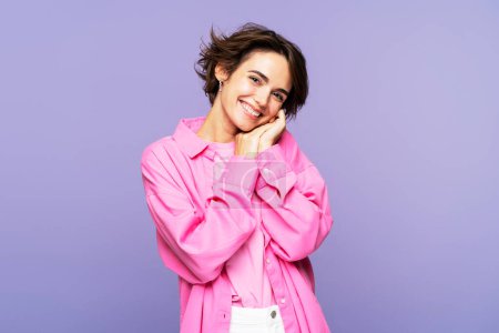 Photo for Portrait photo of an attractive, dreamy, cute young brunette hair woman, dressed in pink clothes, with her hands folded, posing isolated on a lilac background, looking into the camera - Royalty Free Image