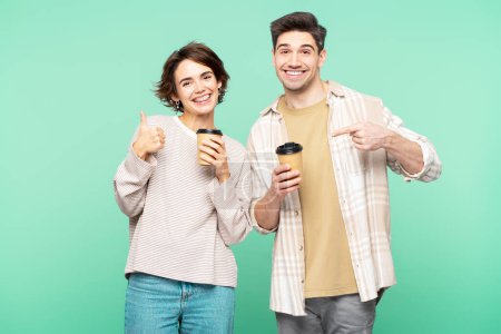 Photo for Portrait photo of cheerful, happy people, holding paper coffee cups and making recommending signs, posing isolated on a turquoise background, looking into the camera - Royalty Free Image