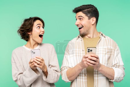 Photo for Portrait photo of smiling, shocked people holding mobile phones, looking each other, and screaming, isolated on a teal background. Online shopping concept - Royalty Free Image