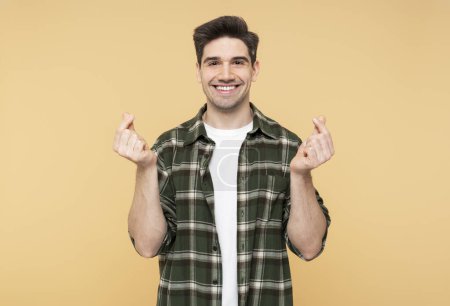 Photo for A portrait of a confident, attractive man displaying the Korean heart sign, affection expression, isolated on a yellow background, looking into the camera - Royalty Free Image