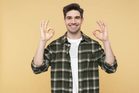 Photo for Portrait photo of a handsome, confident man making an okay gesture, posing against an isolated yellow background, and looking at the camera - Royalty Free Image