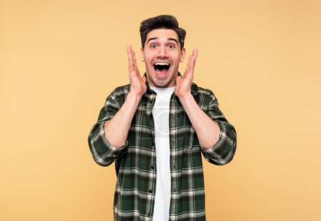 Portrait of a handsome shocked man, shouting with his mouth wide open, gesturing with his hands, posing against an isolated yellow background, and looking at the camera
