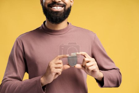 Photo for Happy handsome African American man holding pacemaker looking at camera closeup. Patient showing cardioverter defibrillator standing isolated on yellow background. Concept of health care, support - Royalty Free Image