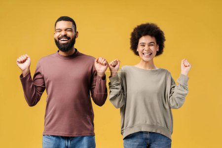 Photo for Smiling, attractive African American couple winners, gesturing with closed eyes rejoicing, win money standing isolated on yellow background. Victory concept - Royalty Free Image