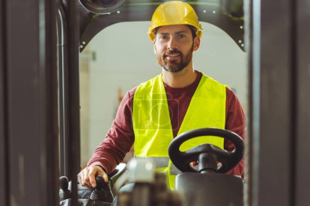 Photo for Smiling, handsome, bearded man, cameraman wearing hard hat, driving car, forklifts behind helm, looking at camera. Concept of distribution, transportation - Royalty Free Image