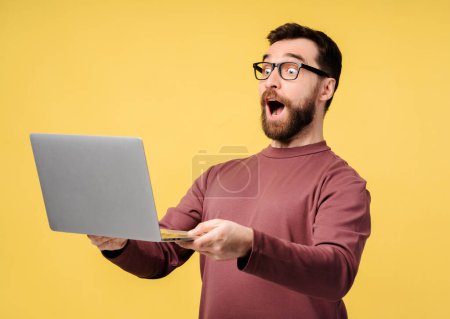 Excited amazed man using laptop, high speed internet, connection isolated on yellow background. Attractive student holding computer preparing for exam, online shopping