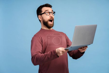 Portrait of excited man using laptop, high speed internet, connection isolated on blue background. Attractive student holding computer preparing for exam, online shopping