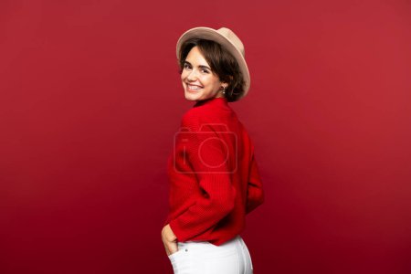 Téléchargez les photos : Portrait de belle Française souriante portant un chapeau élégant regardant la caméra isolée sur fond rouge. Concept de beauté naturelle - en image libre de droit