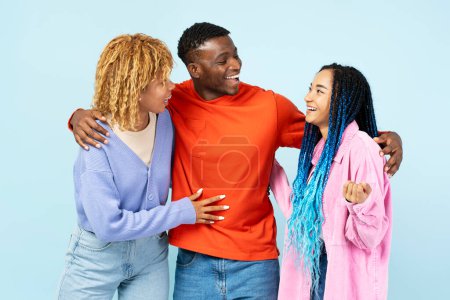 Photo for Group of young smiling friends wearing stylish clothing hugging, standing together isolated on blue background. Positive lifestyle, friendship concept - Royalty Free Image