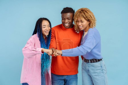 Photo for Portrait of smiling positive African American friends in casual colorful outfit giving fist bump, hugging isolated on blue background. Friendship concept - Royalty Free Image