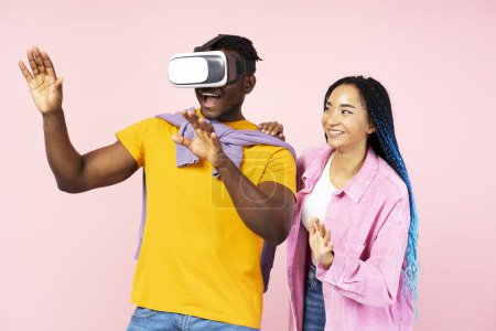 Téléchargez les photos : Couple professionnel de joueurs afro-américains portant des lunettes VR jouant au jeu vidéo, isolé sur fond rose. Concept innovant, simulation 3D - en image libre de droit