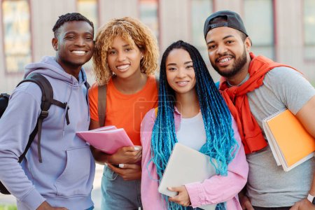 Téléchargez les photos : Groupe de souriants divers amis afro-américains en vêtements décontractés colorés regardant la caméra près du campus universitaire sur la rue. Heureux étudiants à l'extérieur. Concept d'éducation, de communication, de rencontre - en image libre de droit