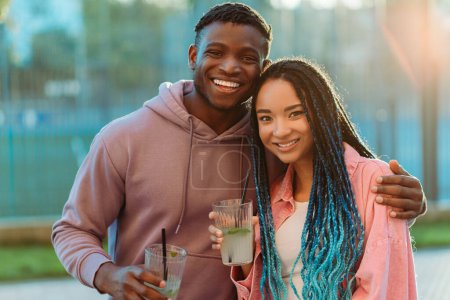 Téléchargez les photos : Jeune couple afro-américain souriant amoureux, homme et femme, amis tenant des cocktails dans la rue, regardant la caméra à l'extérieur. Concept d'amour, relation - en image libre de droit