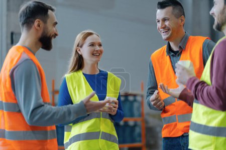 Photo for Group of workers wearing workwear holding cup with coffee talking, coffee break, standing together in warehouse. Teamwork concept, communication, logistic - Royalty Free Image