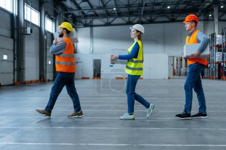 Photo for Group of workers, professional loaders, holding boxes, carrying them to warehouse. Young men and woman wearing safety helmet and workwear. Concept of logistics, delivery, distribution - Royalty Free Image