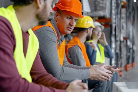 Photo for Attractive, confident factory foreman, worker, man wearing hard hat and work wear talking to colleagues while working in warehouse. Career concept, teamwork - Royalty Free Image