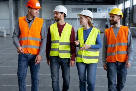 Photo for Successful, attractive engineers, workers wearing hard hats walking around warehouse, talking, discussing something important, break. Concept of industry, logistics - Royalty Free Image