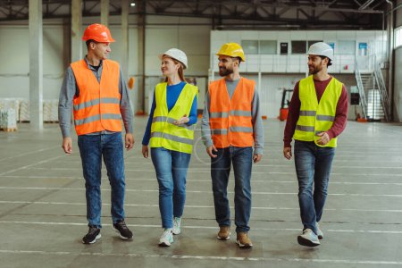 Photo for Successful warehouse managers wearing in working wear vest and hard hats walking through warehouse distribution center discussing about productivity. Good teamwork concept - Royalty Free Image