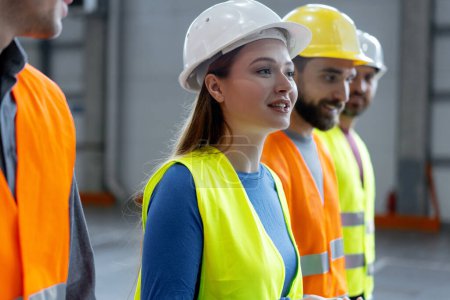 Photo for Happy engineers, smiling female worker wearing protective helmets talking with colleagues, walking in warehouse. Cooperation, teamwork concept - Royalty Free Image