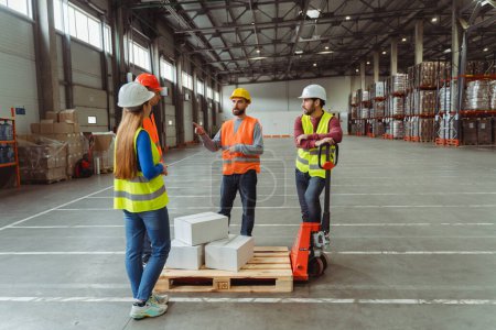 Photo for Group of happy managers, workers wearing safety helmet and vest loading boxes on pallet truck, work in warehouse, distribution. Concept of logistics, storage, teamwork - Royalty Free Image