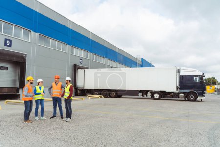 Photo for Group of successful workers, managers, engineers in hard hats standing on the street near cargo terminal, copy space, mockup, talking. Concept of transportation, business - Royalty Free Image
