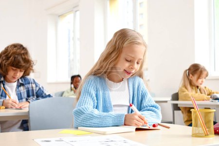 Photo for Smiling school girl taking notes in notebook while sitting in the classroom. Education concept. Back to school - Royalty Free Image