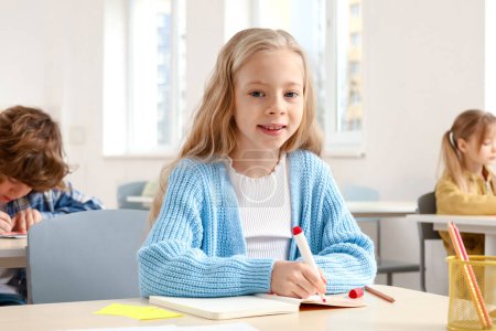 Téléchargez les photos : Portrait d'une écolière souriante prenant des notes en classe tout en regardant la caméra. Concept d'éducation. Retour à l'école - en image libre de droit