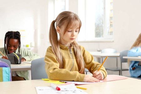 Photo for Little girl doing exercise in the notebook with classmates on the background in classroom. Education concept. Back to school - Royalty Free Image