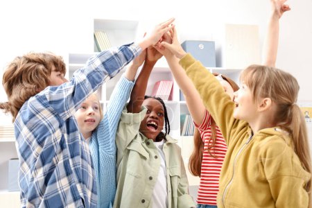 Foto de Niños felices poniendo sus manos juntas mientras están de pie en la escuela. Unidad, concepto de amistad - Imagen libre de derechos