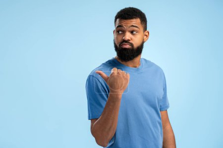 Junger afroamerikanischer Mann in lässigem T-Shirt, während er mit erhobenem Daumen zur Seite zeigt, isoliert auf blauem Hintergrund. Lebensstil-Konzept der Menschen