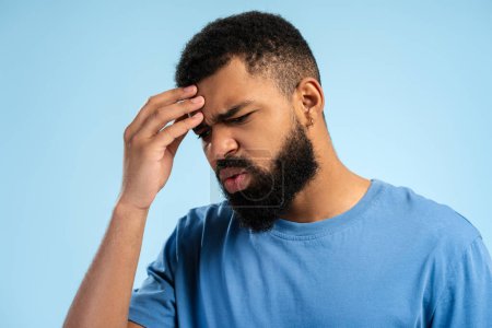 Photo for Portrait of casual bearded African American man with headache posing in studio, isolated on blue background. People lifestyle concept - Royalty Free Image