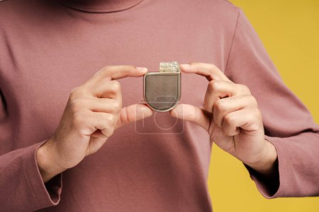 Man demonstrating implantable cardioverter defibrillator, close up, isolated om yellow background. Health care and heart concept