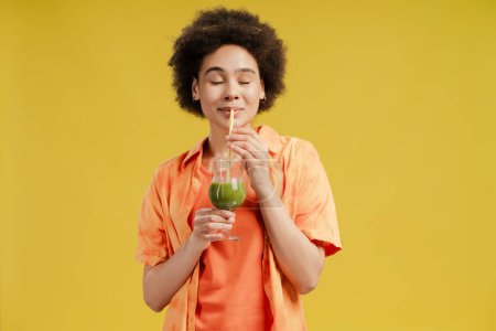 Téléchargez les photos : Femme afro-américaine positive posant avec un cocktail d'été en studio, profitant de la boisson exotique, isolée sur jaune. Vacances, concept de fête d'été - en image libre de droit
