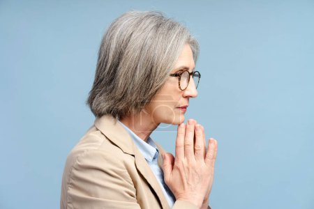 Senior sad businesswoman in eyeglasses looking away and thinking problems isolated on blue background. Stress, depression concept