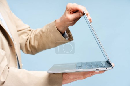 Foto de Las manos de la mujer mayor ordenador portátil de apertura de trabajo en línea aislado sobre fondo azul. Exitoso escritor de 60 años sosteniendo la computadora. Concepto tecnológico - Imagen libre de derechos