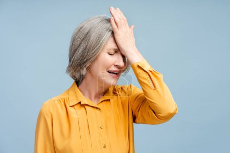 Porträt einsame nervöse Seniorin mit Kopfschmerzen, Migräne, benötigen medizinische Behandlung isoliert auf blauem Hintergrund. Unzufriedene Frau wurde entlassen. Stress, Depression, Schmerz 
