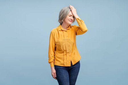 Nervous senior woman having headache, migraine, need medical treatment isolated on blue background. Unhappy female fired from job. Stress, depression, pain concept