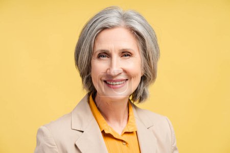 Portrait of happy senior gray haired woman, politician leader looking at camera isolated on yellow background. Successful business, career