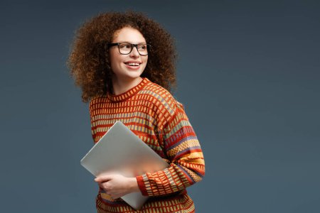 Téléchargez les photos : Portrait de femme souriante, pigiste utilisant ordinateur portable tenant l'ordinateur regardant loin isolé sur fond gris. Concept de technologie en ligne - en image libre de droit