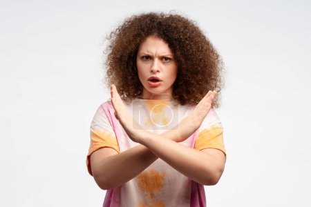 Photo for Serious, angry, young woman with curly hair showing with hands no gesture, stop sign, arms crossed, looking at camera standing isolated on white background. Concept of negative emotions - Royalty Free Image