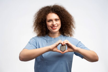 Photo for Attractive smiling young woman wearing blue t shirt holding pacemaker looking at camera isolated on white background, closeup. Concept of health care, treatment of heart - Royalty Free Image