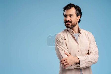 Photo for Positive young man posing in casual while holding hands crossed, looking away, isolated on blue. Copy space. Shopping, sale concept. Advertisement concept - Royalty Free Image