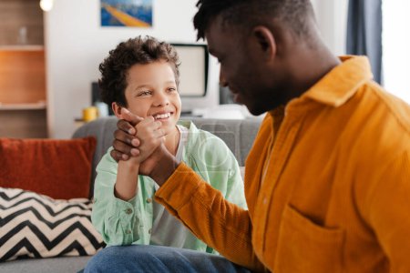 Photo for Smiling, positive family, little boy and his African American father spending time together, talking, sitting on comfortable sofa. Concept of team, love, relationship, parenthood - Royalty Free Image