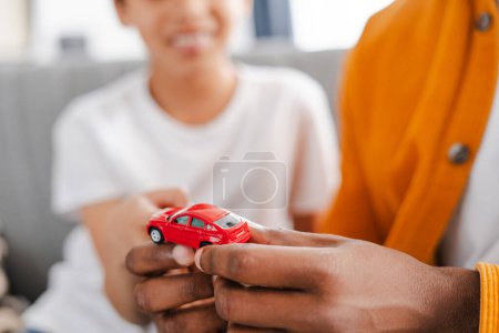 Photo for Closeup, African American man playing with his son, holding small red car toy, selective focus on his hands. Childhood concept - Royalty Free Image