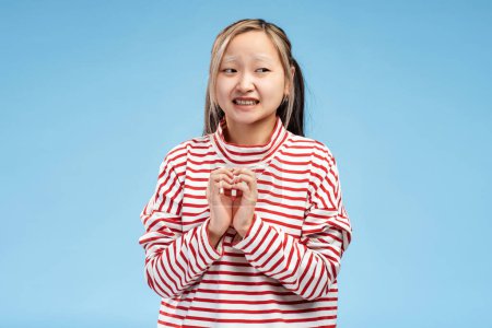 Téléchargez les photos : Portrait de fille asiatique inquiète tenant la main détournée, avoir peur, posant en studio, isolé sur fond bleu. Concept de publicité - en image libre de droit