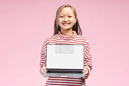 Photo for Portrait of pretty Asian student holding open laptop, screen with copy space, looking at camera, isolated on pink. Online technology, education concept - Royalty Free Image