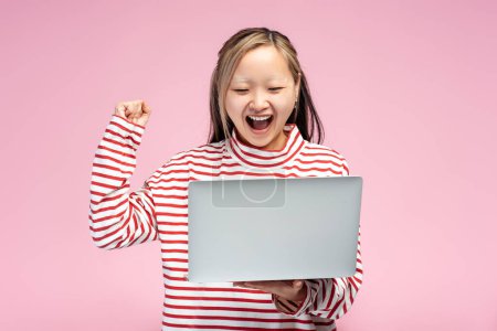 Photo for Portrait of excited Asian student girl screaming looking at laptop screen holding hand up, isolated on pink background. Online technology, education concept - Royalty Free Image