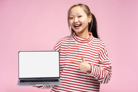 Porträt eines glücklichen asiatischen Studentenmädchens, das mit hochgereckten Daumen in die Kamera blickt und Laptop mit Bildschirm für Kopierraum hält, isoliert auf rosa. Online-Technologie, Bildungskonzept