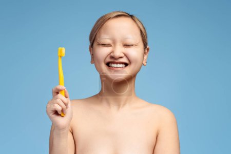 Foto de Portrait of smiling Asian girl with closed eyes posing with toothbrush, isolated on blue background. Dental healthcare concept - Imagen libre de derechos