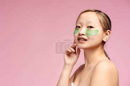 Téléchargez les photos : Portrait de fille asiatique souriante regardant la caméra avec des bandeaux sur le visage, isolé sur rose,. Espace de copie. Concept de produit d'entretien publicitaire. Soins de la peau - en image libre de droit